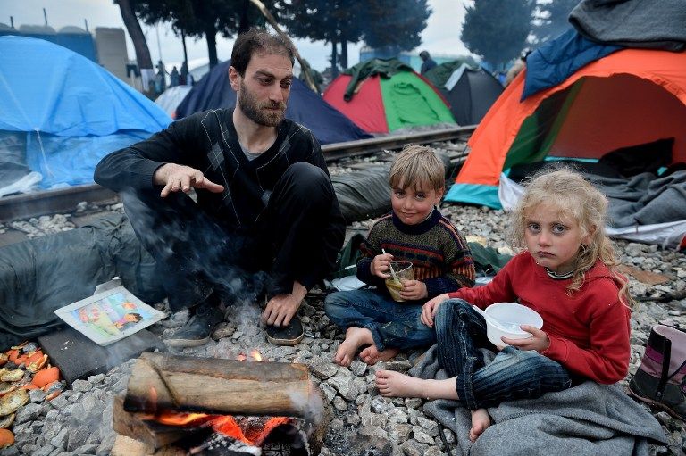 A syrian father and two of his children get warm by a fire between train tracks at the Greek-Macedonian border near the Greek village of Idomeni on March 10, 2016, where thousands of refugees and migrants are trapped by the Balkan border blockade. The German and Greek leaders blasted Balkan countries for shutting their borders to migrants ahead of an EU ministers meeting on March 10. Greek authorities said there were 41,973 asylum seekers in the country, including some 12,000 stuck at Idomeni on the closed Macedonian border. / AFP / DANIEL MIHAILESCU