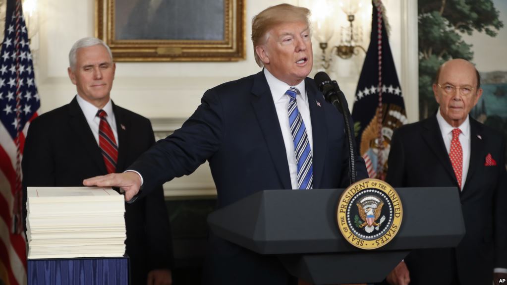 President Donald Trump reaches to touch a copy of the budget as he makes a statement in the Diplomatic Room of the White House in Washington, Friday, March 23, 2018. With Trump are Vice President Mike Pence, left, and Commerce Secretary Wilbur Ross.  (AP Photo/Pablo Martinez Monsivais)