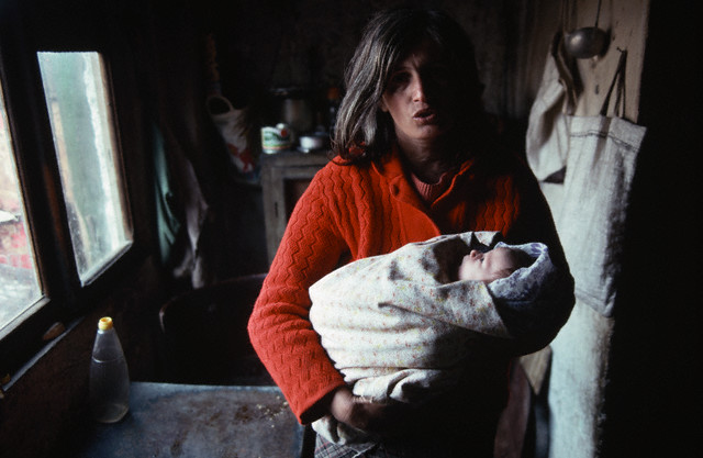 March 1992, Tirane, Albania --- A woman holds her tightly wrapped baby in a dark kitchen in a poor neighborhood in Albania's capitol city. --- Image by Â© Peter Turnley/CORBIS