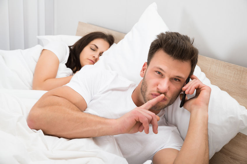 Man Talking Privately On Cellphone While His Wife Sleeping On Bed