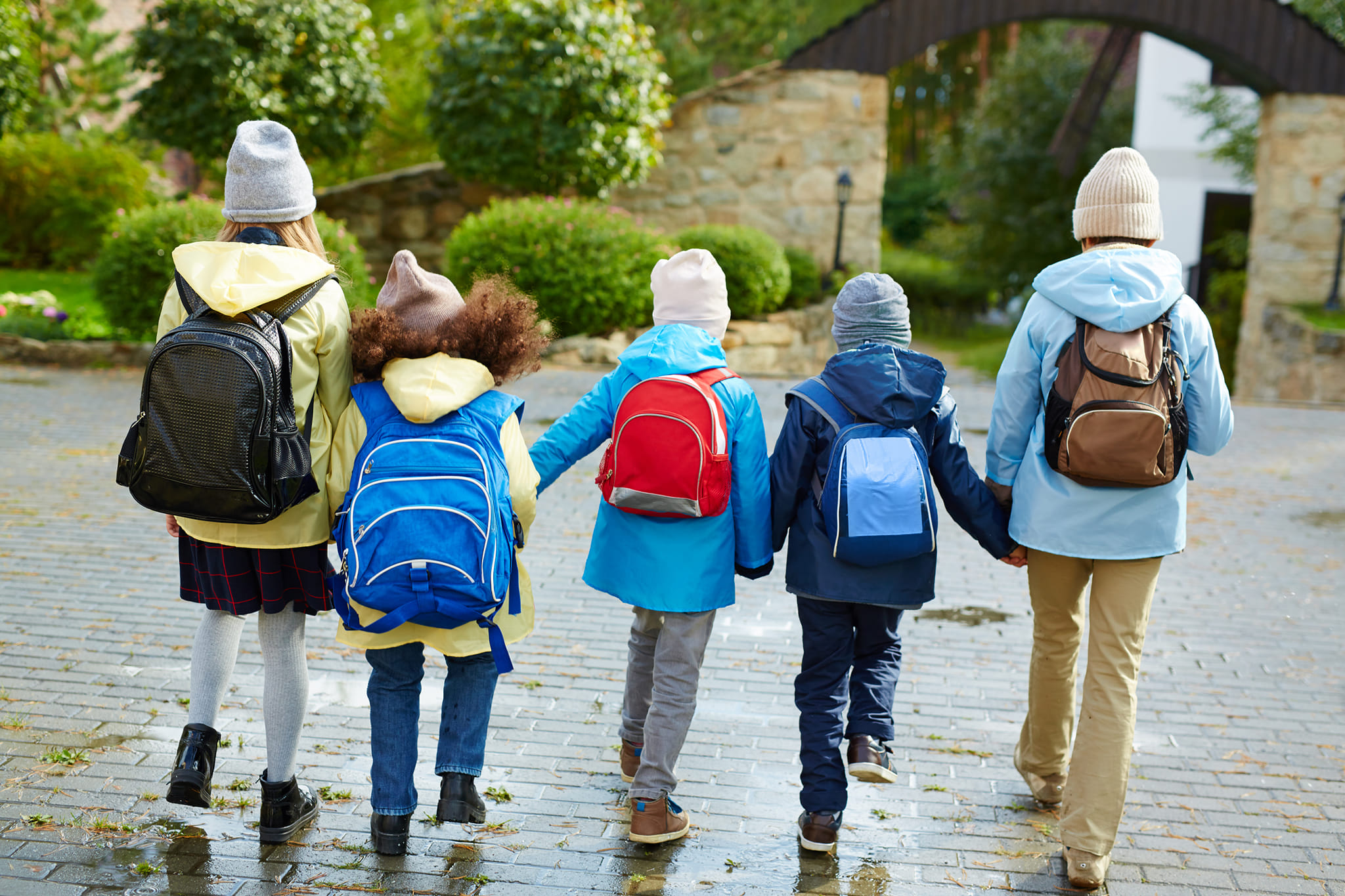 Schoolkids in casualwear with rucksacks behind backs holding by hands while going to school