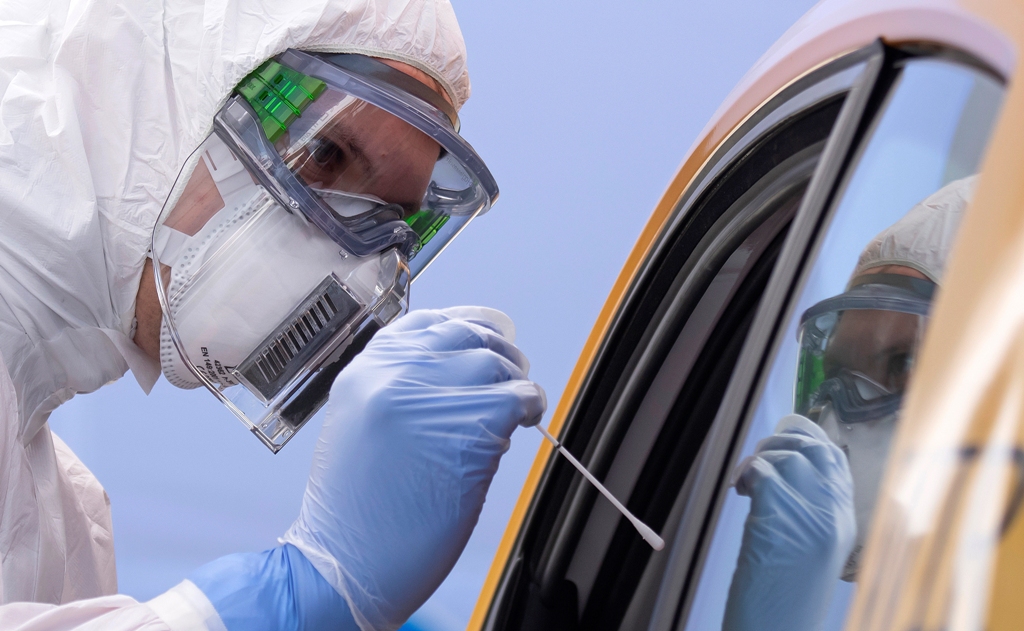 FILE - In this April 15, 2020, file photo, helper of the German Red Cross DRK in protective suit, left, takes a smear from a patient in his car during the official opening of a drive-thru COVID-19 testing center at the fair ground in Dresden, eastern Germany. As the restrictions to avoid the spreading of the coronavirus are eased, Chancellor Angela Merkel has pointed to South Korea as an example of how Germany will have to improve measures to “get ahead” of the pandemic with more testing and tracking of cases so that the rate of infections can be slowed. (AP Photo/Jens Meyer, File)