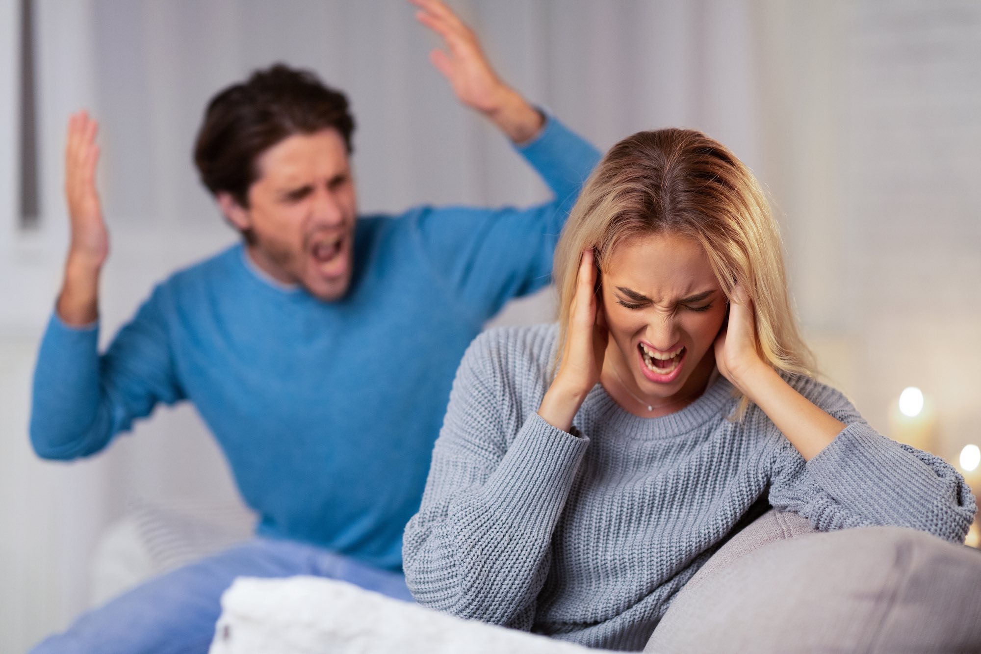 Family Abuse. Angry Boyfriend Shouting At Girlfriend Covering Ears Sitting On Couch Indoor. Selective Focus